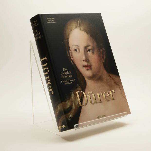 A hardcover art book titled 'Dürer: The Complete Printmaker' resting on a dark textured surface. The cover features a classical portrait painting of Albrecht Dürer with his name in large gold lettering.