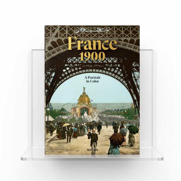 A book cover titled "France 1900: A Portrait in Color" showing a vintage scene viewed through the iron arch of the Eiffel Tower, with people walking in the foreground and the title in large gold lettering. The publisher name TASCHEN is visible at the bottom.