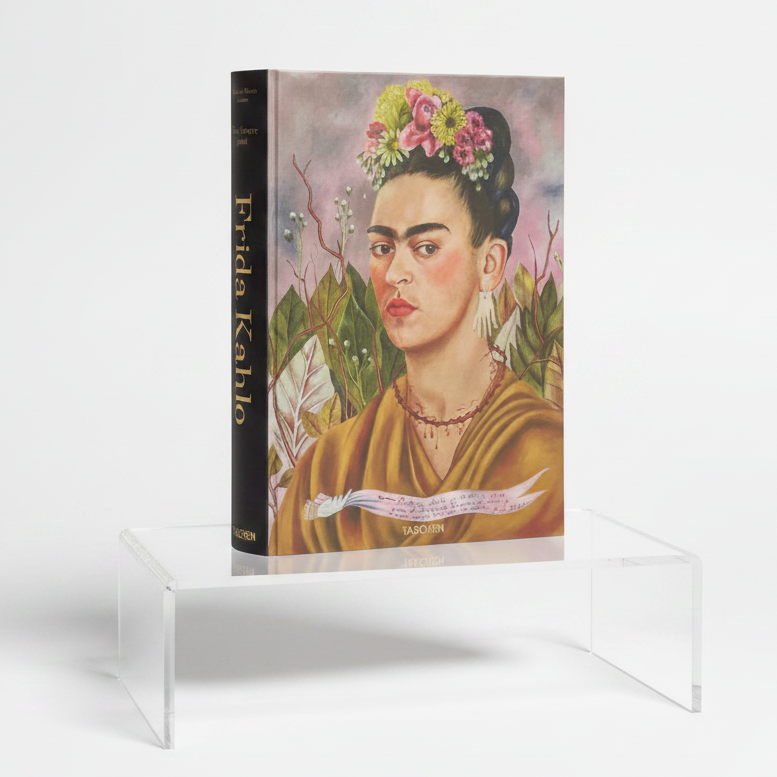 A hardcover art book titled 'Frida Kahlo' by Taschen, featuring a colorful painted portrait of Frida Kahlo on the cover and a dark spine, displayed on a purple surface against a black background.