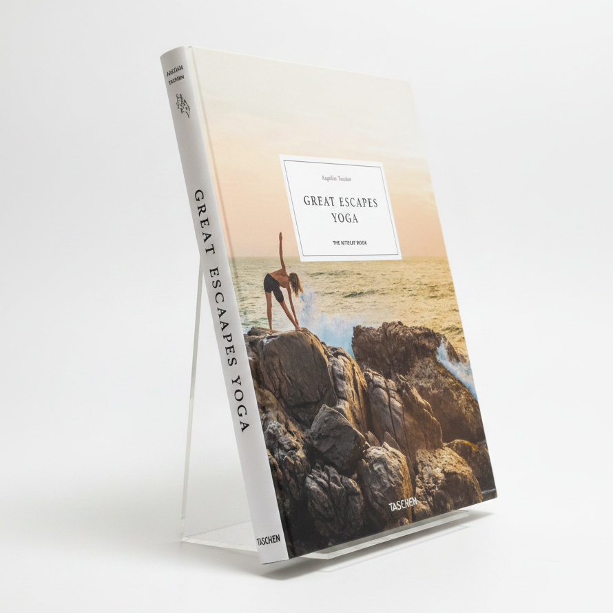 The front cover of the book 'Great Escapes Yoga' by Angelika Tschiekern, published by Taschen. The cover features a photograph of a woman in a yoga pose on a rocky coastline at sunset, with a white title box in the center.