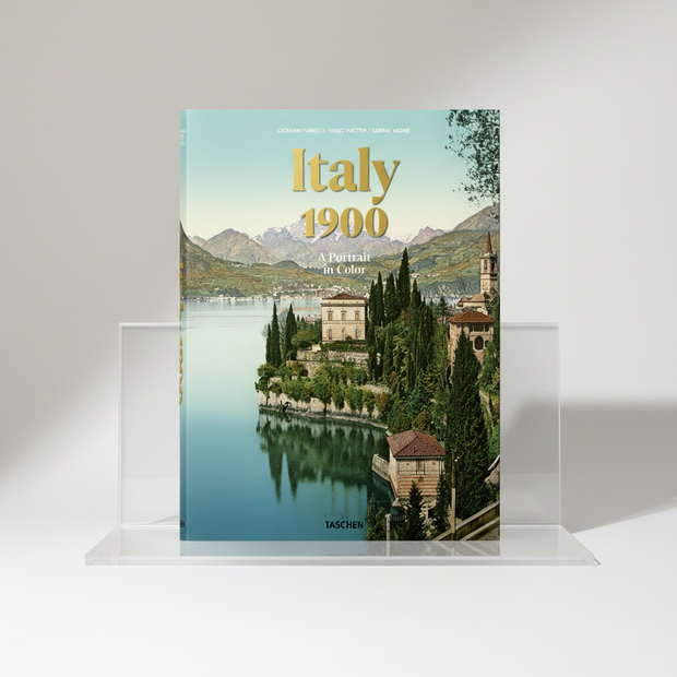 The front cover of the book 'Italy 1900: A Portrait in Color' by Giovanni Fannelli, Marc Galterix, and Sabine Angüe, published by Taschen. The cover features a vintage-style scenic photograph of a lakeside town with mountains in the background, under a pale blue sky, with the title in large gold letters.